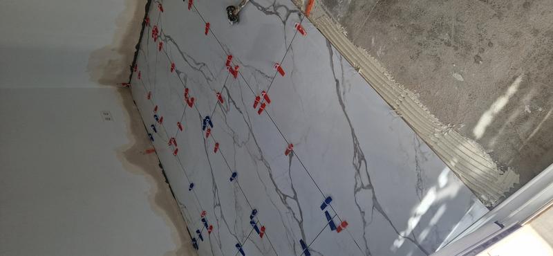 Verlegung des neuen keramischen Bodens in Marmoroptik auf der bereits abgedichteten Flache, mit Keilen und Nivellierern zur Kontrolle von Fugen und Ebenheit.