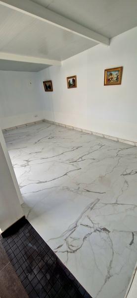 Vista de la habitación tras la reforma, con el nuevo pavimento cerámico imitación mármol terminado y el perímetro rematado, lista para la medición final de radón.